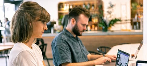 Two young professionals working on laptops in a modern cafe setting.